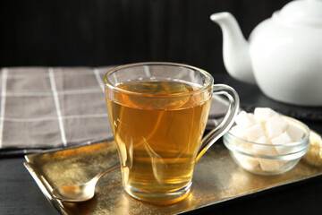 Tasty tea in glass cup, sugar cubes and teaspoon on black wooden table, closeup