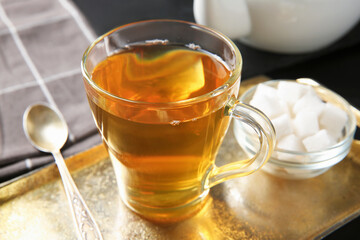 Tasty tea in glass cup, sugar cubes and teaspoon on black table, closeup