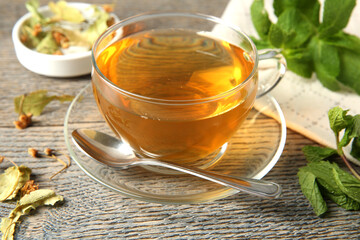 Tasty tea in glass cup, linden, mint and teaspoon on wooden table, closeup