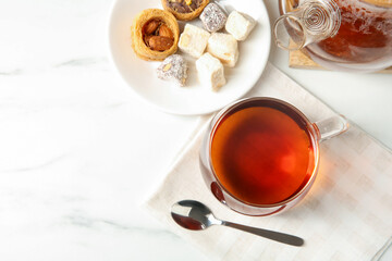 Tasty tea in glass cup, teaspoon, Turkish desserts and teapot on white marble table, flat lay. Space for text