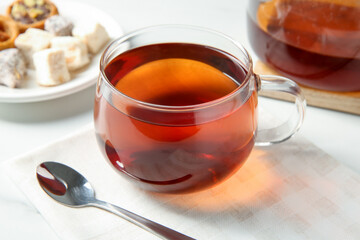 Tasty tea in glass cup and teaspoon on white table, closeup