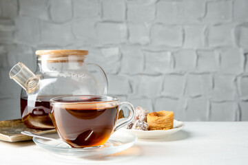 Tasty tea in glass cup, teapot and Turkish desserts on white table against grey textured background, closeup. Space for text