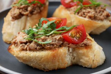 Delicious bruschettas with tuna, tomatoes and arugula on plate, closeup
