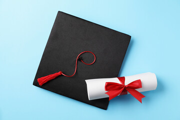Diploma and graduation hat on light blue background, top view