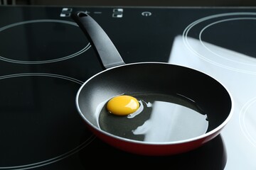 Frying pan with raw chicken egg on cooktop in kitchen, closeup