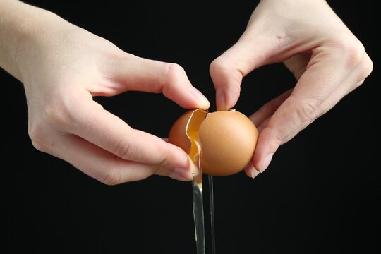 Woman cracking egg on black background, closeup - Powered by Adobe