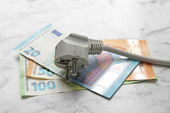 Electrical wire with plug and euro banknotes on white marble table, closeup