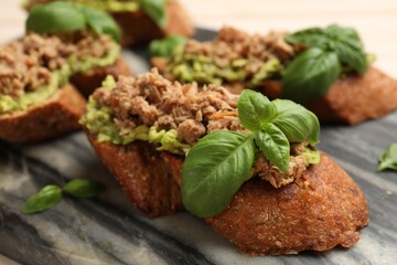 Delicious bruschettas with tuna, avocado and basil on table, closeup