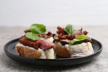Bruschettas with roast beef, cream cheese, basil and sun-dried tomato on grey table, closeup