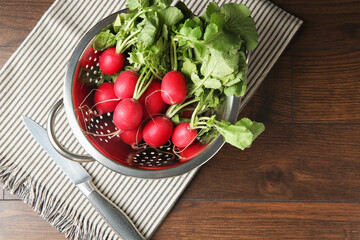 Fresh ripe radishes in colander and knife on wooden table, top view