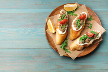 Delicious bruschettas with tuna, cream cheese and tomatoes on light blue wooden table, top view. Space for text