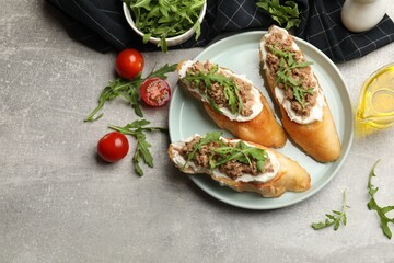 Delicious bruschettas with tuna, tomatoes, oil and arugula on grey table, flat lay. Space for text