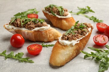 Delicious bruschettas with tuna, tomatoes and arugula on grey table, closeup