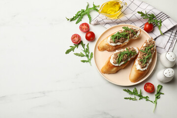 Delicious bruschettas with tuna, tomatoes, oil and arugula on white marble table, flat lay. Space for text