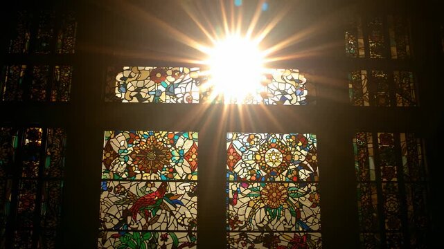 Starting sunbeam piercing stained glass in chapel, brightening floral mandalas and bird motif