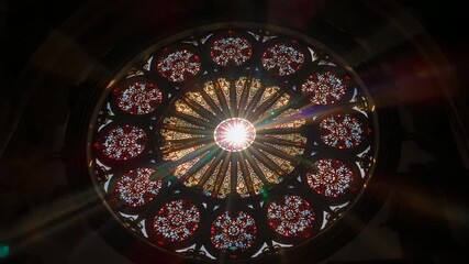 Sunlight shifting behind stained rose window emitting sunburst lens flares across cathedral nave - Powered by Adobe