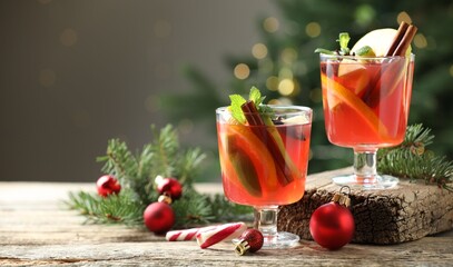 Tasty punch drink in glasses, spices and Christmas decor on wooden table against background with blurred lights, space for text. Bokeh effect