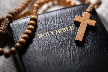 Praying with wooden rosary beads crucifix cross on Holy Bible background