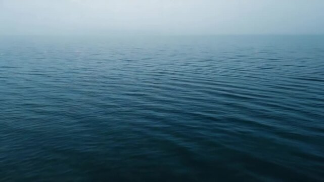 Forming gentle ripples, blue water undulating across open sea under overcast sky with horizon line