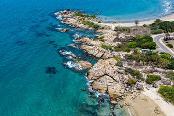 An aerial view of Rose Bay in Bowen, Queensland, reveals a stunning tropical coastline with turquoise waters, golden sand, and rocky headlands. The scene highlights coastal beauty and vibrant color.