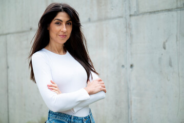 Beautiful brunette woman standing with cross arms outdoor on a concrete wall background 