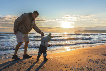 Dad walking toddler on beach in sunset light. Family joy by the sea.