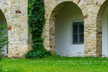 Naklejka premium close up of architectural details, old stone wall with arched opening and green ivy