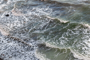 Foamy waves on greenish sea, rhythm and texture. Sea foam closeup.