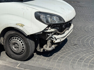 Front part of a white van damaged after a minor accident on a city street. Concept of road safety, traffic and urban life.