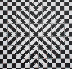 Abstract geometric optical illusion featuring a black and white checkered pattern with layered triangular shapes forming a star-like center. strong visual depth and dynamic symmetry effect.