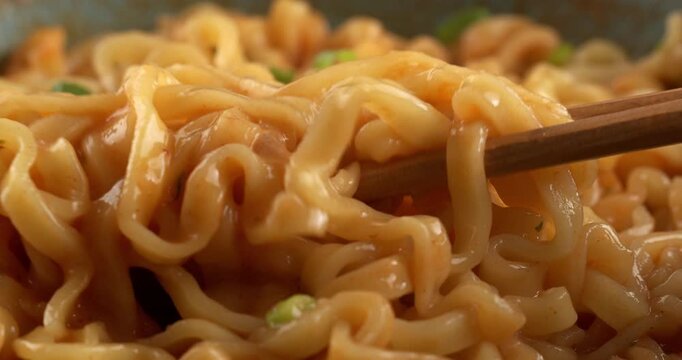 Korean spicy ramyeon noodle soup, with spices and green onions. Chopsticks pick up noodles.