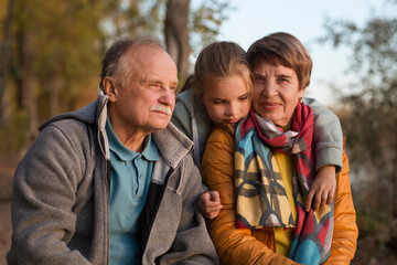 Little child girl hugs grandpa and grandmother On Walk iin nature on a sunny autumn day. Concept of friendly family.
