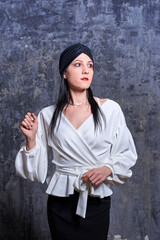 In a dark room stands a beautiful girl with long hair, dressed in a black leather skirt and a white blouse. Her outfit is designed in a business style. This is the image of a business woman.