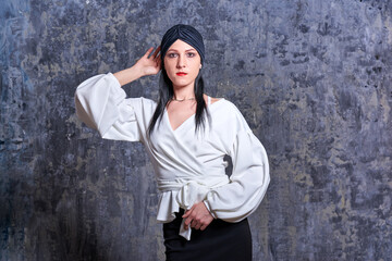 In a dark room stands a beautiful girl with long hair, dressed in a black leather skirt and a white blouse. Her outfit is designed in a business style. This is the image of a business woman.
