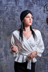 In a dark room stands a beautiful girl with long hair, dressed in a black leather skirt and a white blouse. Her outfit is designed in a business style. This is the image of a business woman.