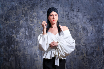 In a dark room stands a beautiful girl with long hair, dressed in a black leather skirt and a white blouse. Her outfit is designed in a business style. This is the image of a business woman.