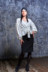 In a dark room stands a beautiful girl with long hair, dressed in a black leather skirt and a white blouse. Her outfit is designed in a business style. This is the image of a business woman.