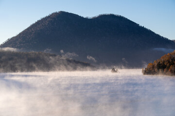 A gentle mist flows over the lake surface in the quiet of early morning