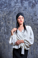 In a dark room stands a beautiful girl with long hair, dressed in a black leather skirt and a white blouse. Her outfit is designed in a business style. This is the image of a business woman.