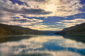 Calm lake between mountains with sunbeams and clouds in the sky in Norway.