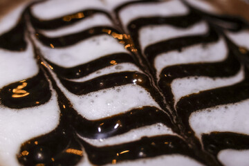 Macro view of creamy white milk foam with delicious dark chocolate syrup in wavy artistic pattern on top of coffee beverage, creating delightful and indulgent texture