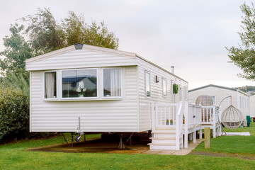 Modern caravan parked in a green space with trees and another structure nearby, suited for relaxing outdoors