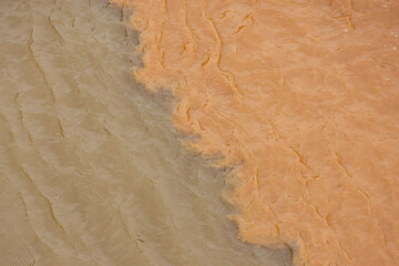 Dramatic aerial view of river confluence, where two bodies of water with mud and clay sediment meet. powerful contrast in color shows mixing flow of nature