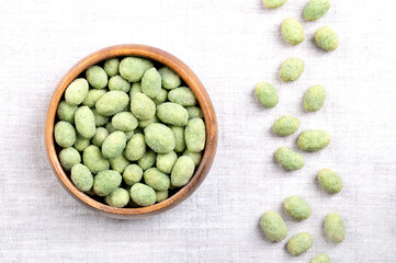 Wasabi peanuts, in a wooden bowl, on linen. Crunchy and spicy snack made of peanut kernels, coated in savory, green wasabi-flavored shell, made of seasoned flour and corn starch, and then roasted.