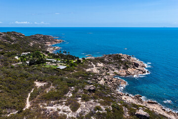 An aerial view of Rose Bay in Bowen, Queensland, reveals a stunning tropical coastline with turquoise waters, golden sand, and rocky headlands. The scene highlights coastal beauty and vibrant color.