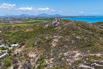 An aerial view of Rose Bay in Bowen, Queensland, reveals a stunning tropical coastline with turquoise waters, golden sand, and rocky headlands. The scene highlights coastal beauty and vibrant color.