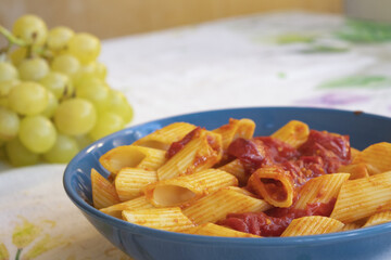 pasta with tomato sauce and prosciutto in blue bowl on white table