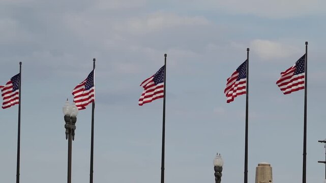 Multiple US flags proudly fly in a line against a soft cloudy sky, symbolizing patriotism, freedom, and national pride.