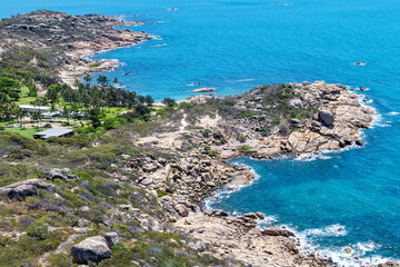 An aerial view of Rose Bay in Bowen, Queensland, reveals a stunning tropical coastline with turquoise waters, golden sand, and rocky headlands. The scene highlights coastal beauty and vibrant color.