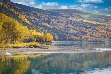 Autumn landscape with colorful forest on the lake shore and mountain backdrop.